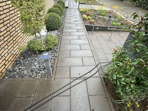 Gehweg entlang eines Hauses während der Reinigung mit Schlauch